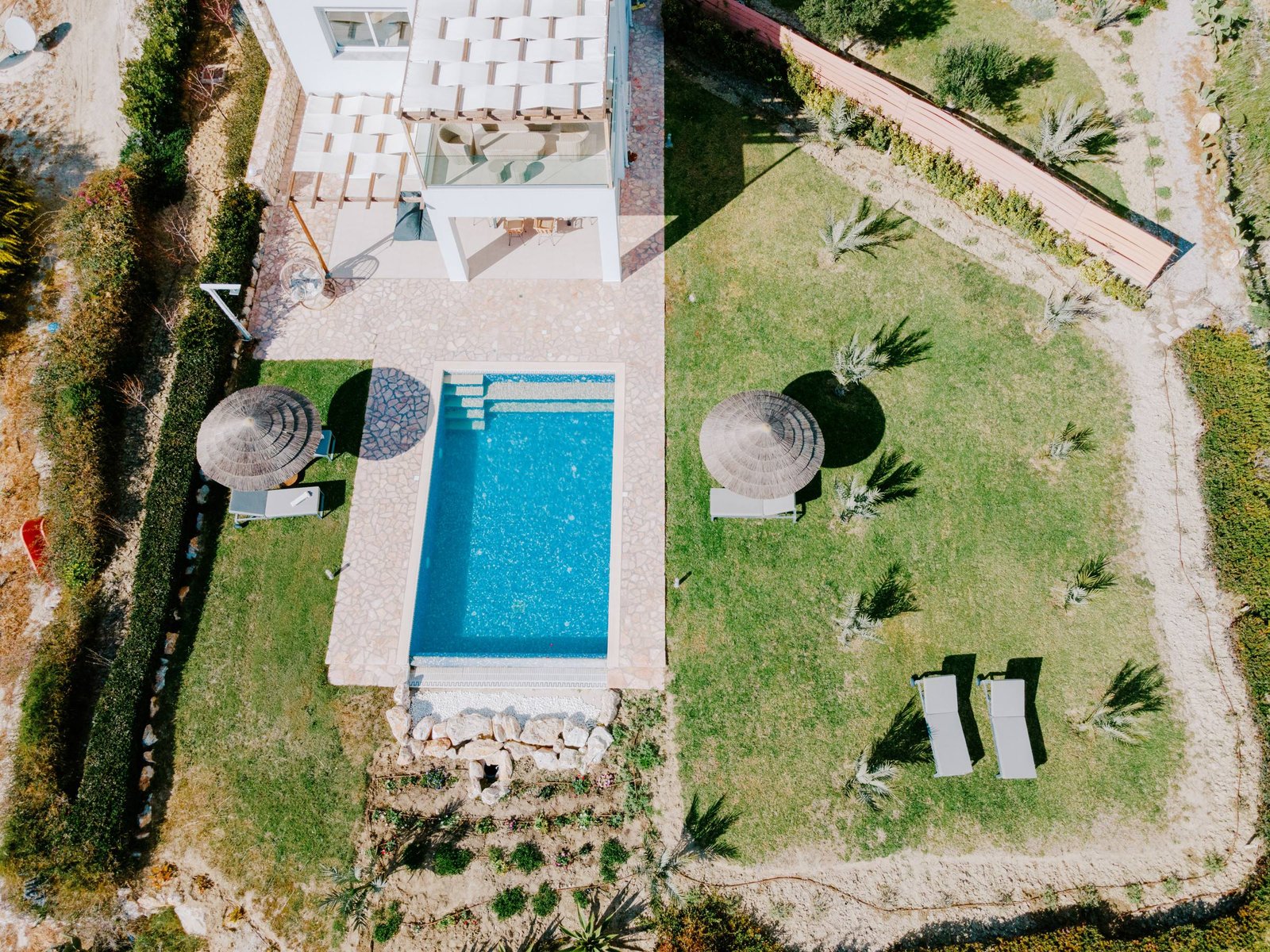Top-down view of a private pool with thatched umbrellas and lawn