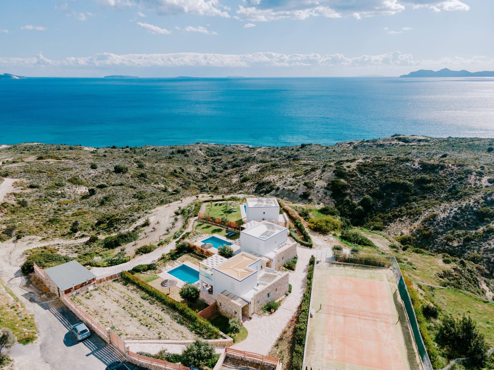 Drone view of the villas, gardens and private tennis court with the sea on the horizon